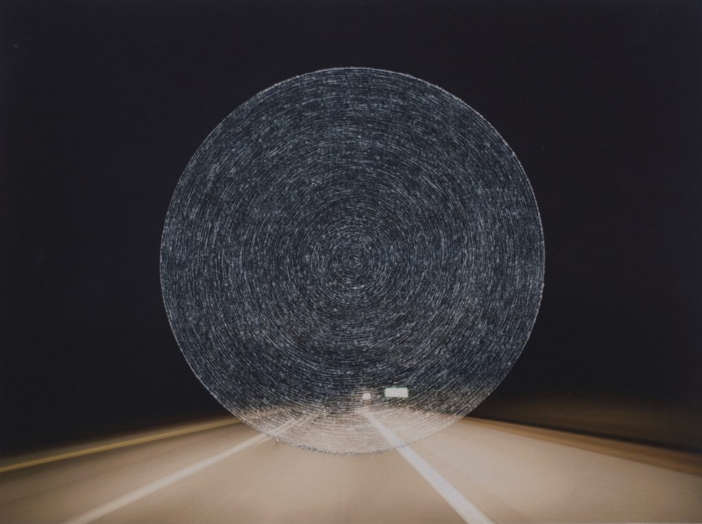 Photograph of a highway at night that has concentric circles scratched into the center of the image.